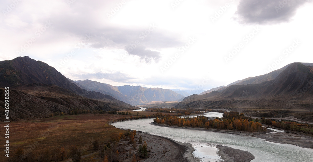 Panoramic shot of a mountain river valley surrounded by mountains with a skylight through storm clouds.