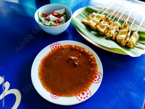 Pork satay served on a blue table, white plate topped with banana leaves and bean dipping sauce. and vegetables in vinegar