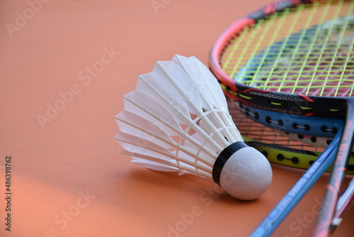 Cream white badminton shuttlecock and racket on red floor in indoor badminton court, copy space, soft and selective focus on shuttlecocks. © Sophon_Nawit