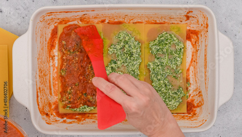 Spinach lasagna recipe. Lsagna noodles layer, spinach mix layer, and marinara sauce layer. Assemble the lasagna, flat lay, woman hands photo