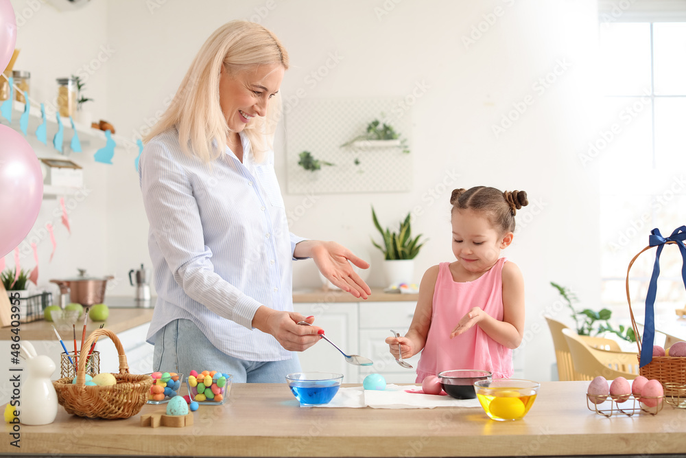 Little girl and her grandmother painting Easter eggs at home