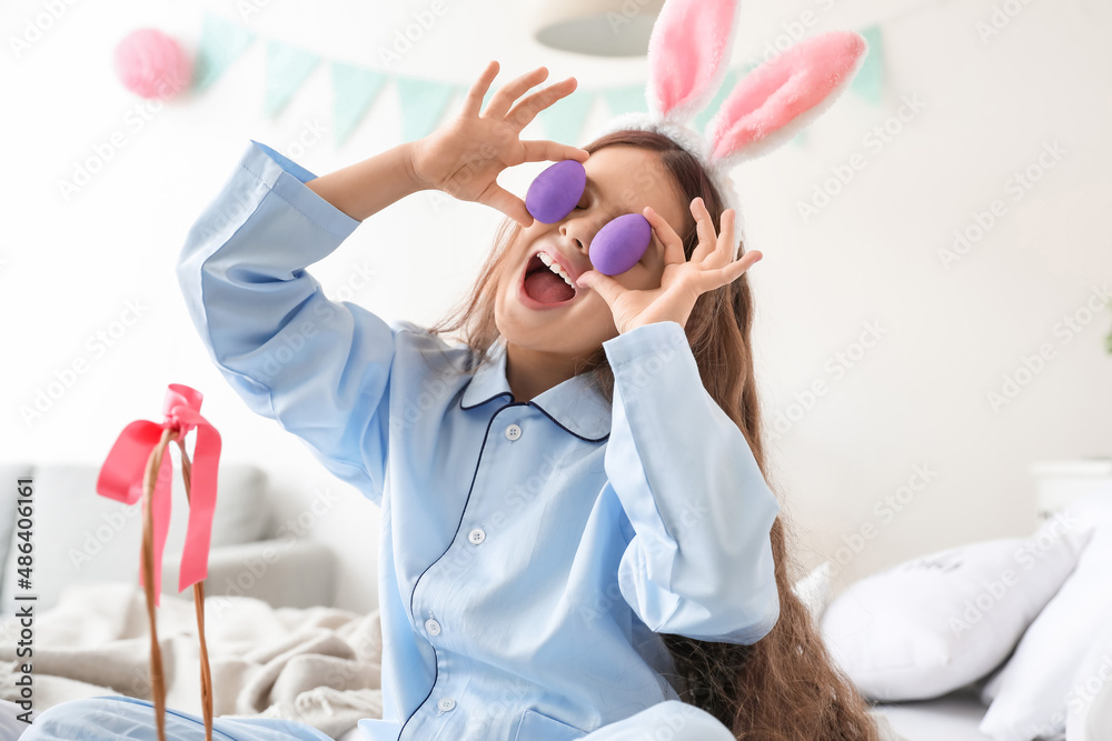 Naklejka premium Cute little girl with bunny ears and Easter eggs in bedroom