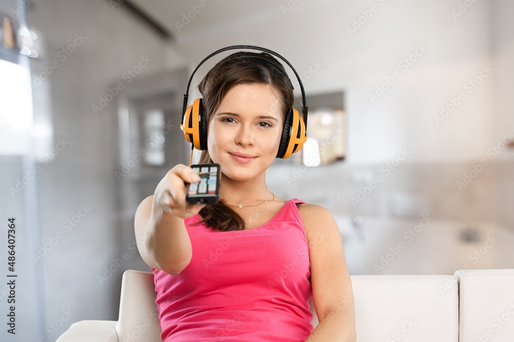 Naklejka premium Portrait of excited young woman watching TV at home holding remote controller