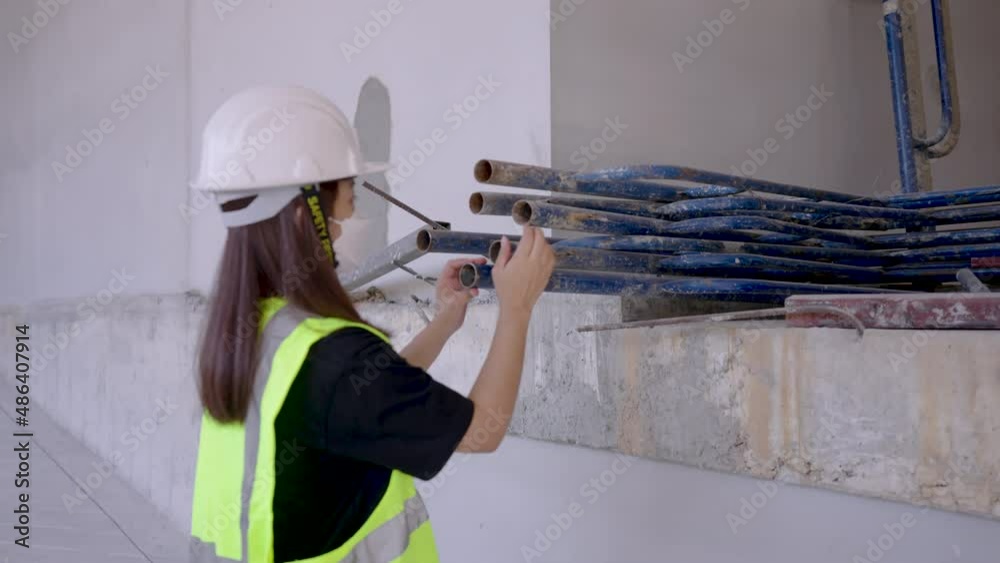 4K, A young female Asian engineer wearing a white safety helmet and reflective green safety vest inspects tools at a construction site. 4K, A young female Asian engineer wearing a white safety helmet and reflective green safety vest inspects tools at a construction site.