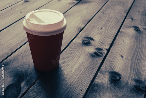 Disposable cup with coffee on a wooden table in a cafe, retro toned photo. Selective focus. © ss404045