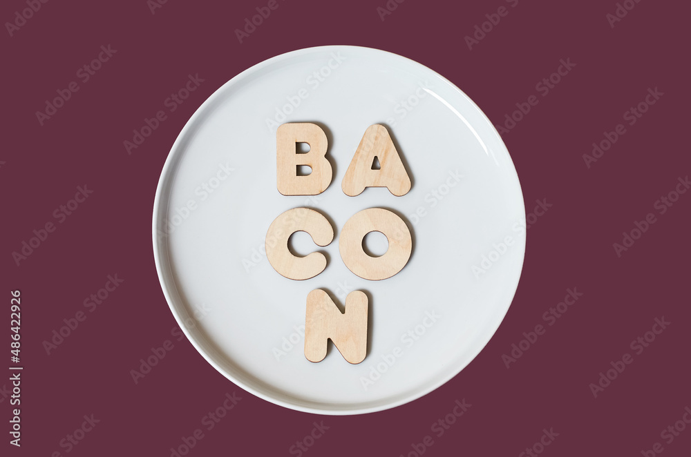 The word Bacon made of wooden letters on a round white plate The word Bacon made of wooden letters on a round white plate