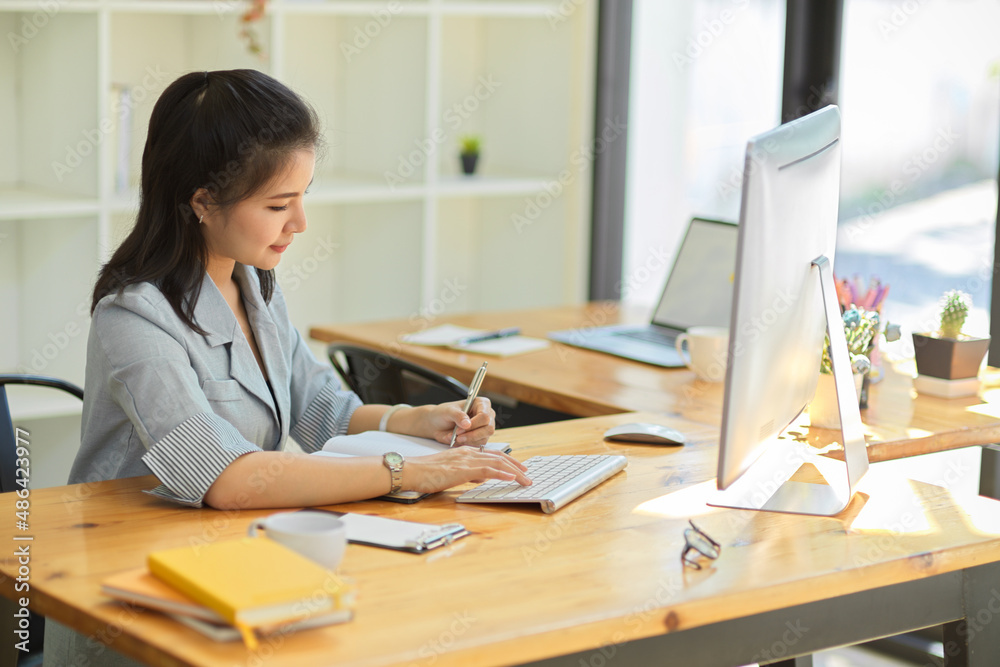 Female manager works on pc computer and take notes on notepad. Female manager works on pc computer and take notes on notepad.