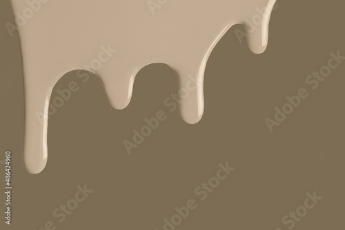 Beige liquid drops of paint color flow down on brown background. Abstract umber backdrop with sand fluid drip