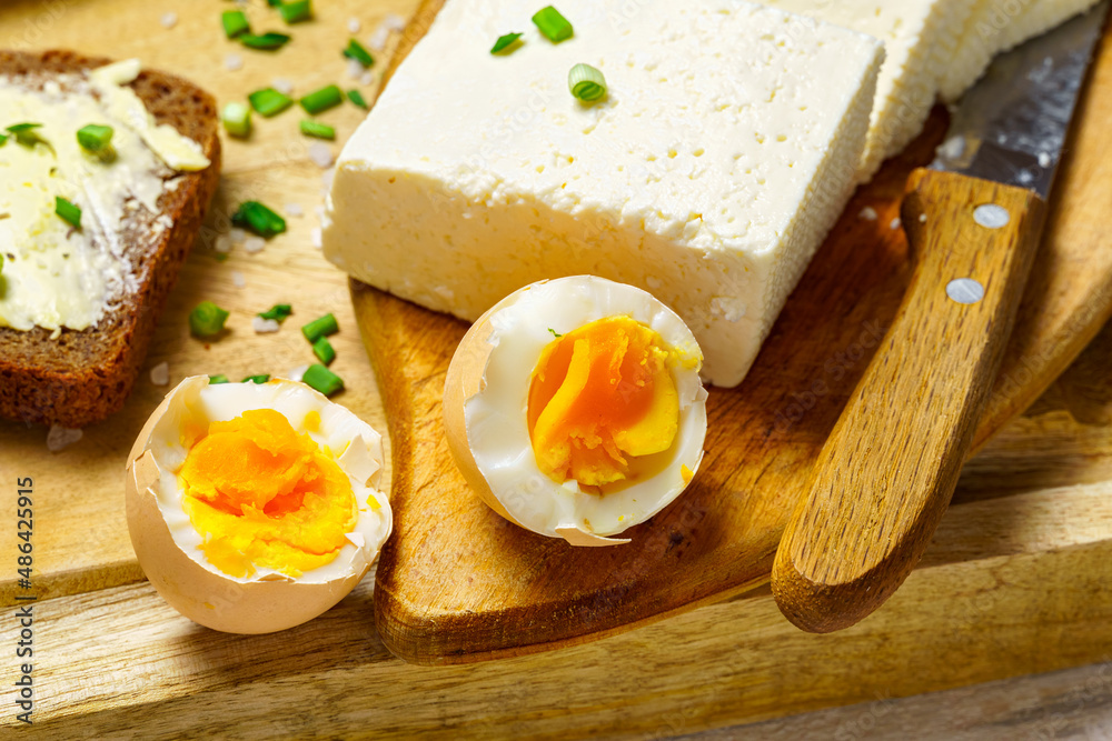 tasty lunch in rural style, healthy food - bread and butter sandwich, feta cheese, eggs, green leek and rye bread, cooked food on a white wooden boards