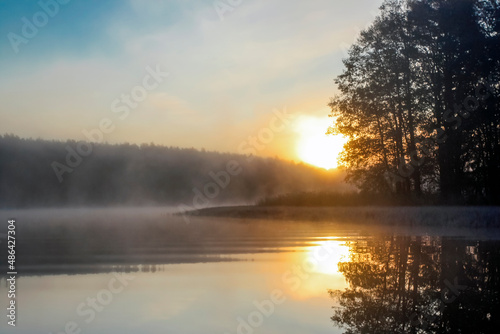 Rising sun in the fog over the water surface of forest lake.