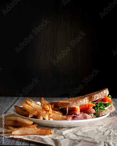 food photography, sandwick  and potatos or french fries in a white plate in a wooden rustic  table with a rustic  dark wooden background