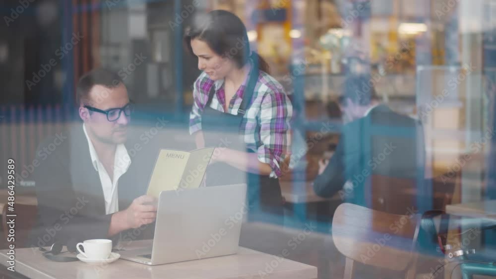 View through window of waitress help businessman with menu order meal in cafe. Realtime View through window of waitress help businessman with menu order meal in cafe. Realtime