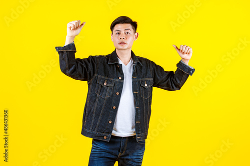 Portrait studio shot Asian young handsome male hipster model wearing casual street denim jacket jeans standing look at camera posing on yellow background.