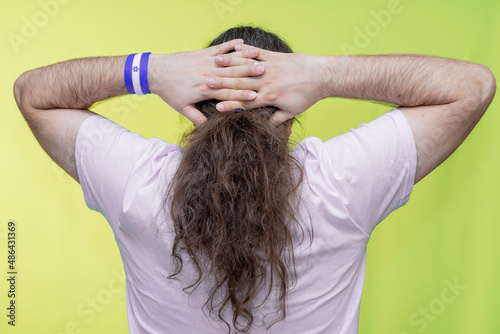 Close-up of a man with long hair holding his hands behind his head. Back view. Bracelet in the colors of the Israel flag.