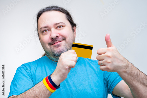 A simple, unshaven middle-aged man holds a plastic card in his hands and rejoices. Bracelet on the wrist in the colors of the German flag.