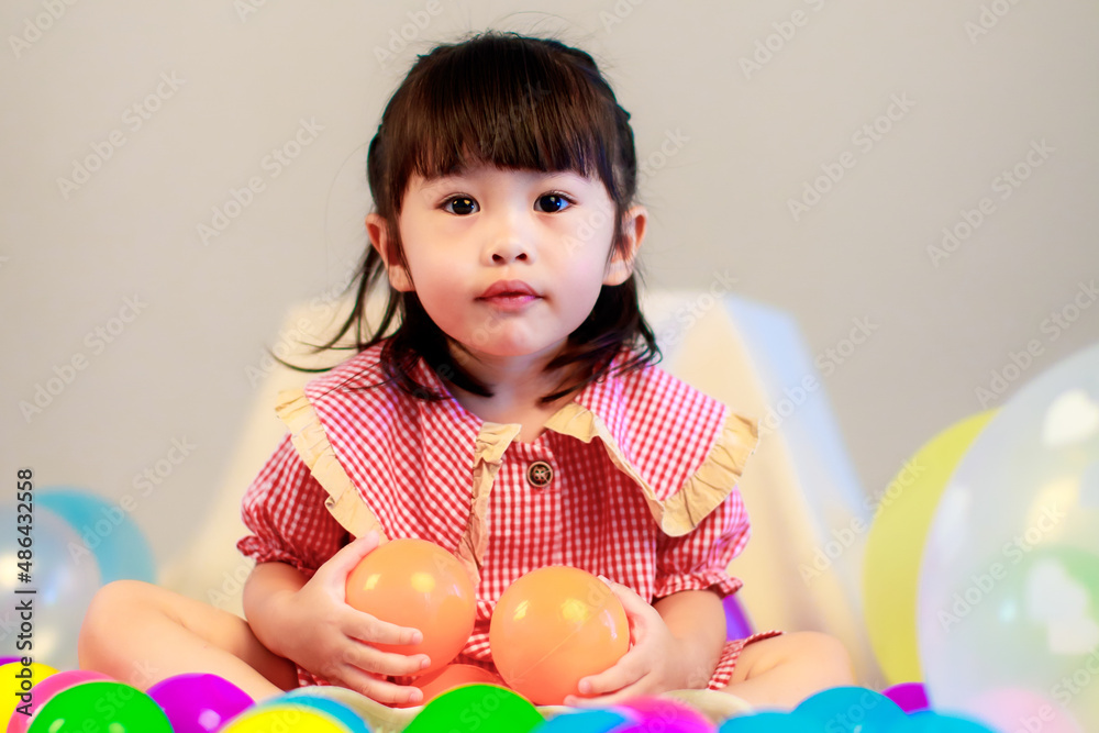 Portrait studio shot of little cute kindergarten preschooler kid girl daughter in red long dress sitting smiling alone on floor playing with colorful helium air party balloons on gray background Portrait studio shot of little cute kindergarten preschooler kid girl daughter in red long dress sitting smiling alone on floor playing with colorful helium air party balloons on gray background