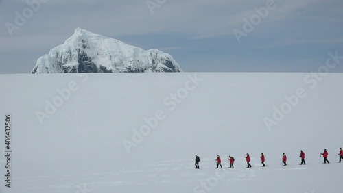 Antarctica Peninsula. A group of people hiking through the snow-capped hills of Antarctica. Scientist research group travel in Antarctica in sunny day. People hikers climbing mountain, team work.