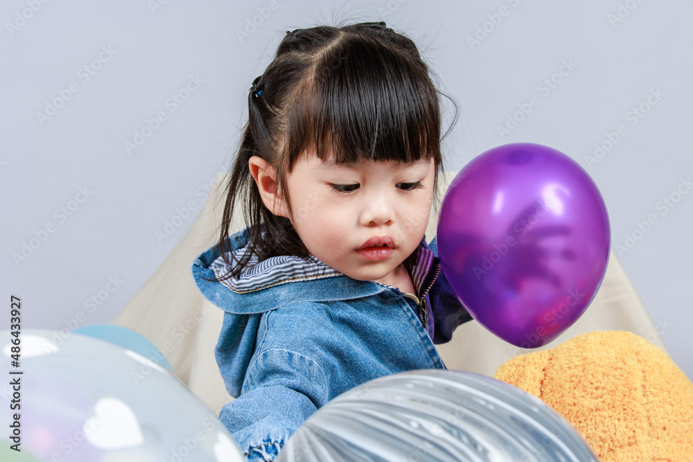 Studio shot of little cute preschooler girl daughter in casual street wears jeans jacket and sneakers sitting smiling teddy bear doll on floor playing with colorful plastic balls on gray background Studio shot of little cute preschooler girl daughter in casual street wears jeans jacket and sneakers sitting smiling teddy bear doll on floor playing with colorful plastic balls on gray background