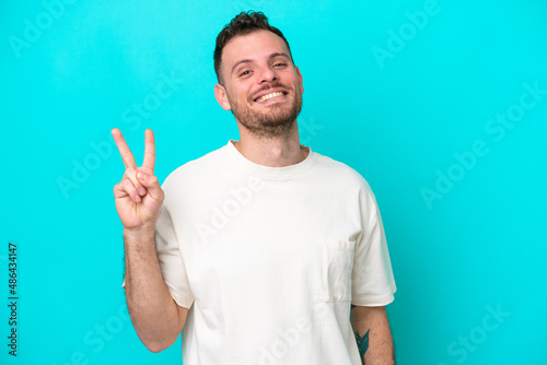 Young Brazilian man isolated on blue background smiling and showing victory sign