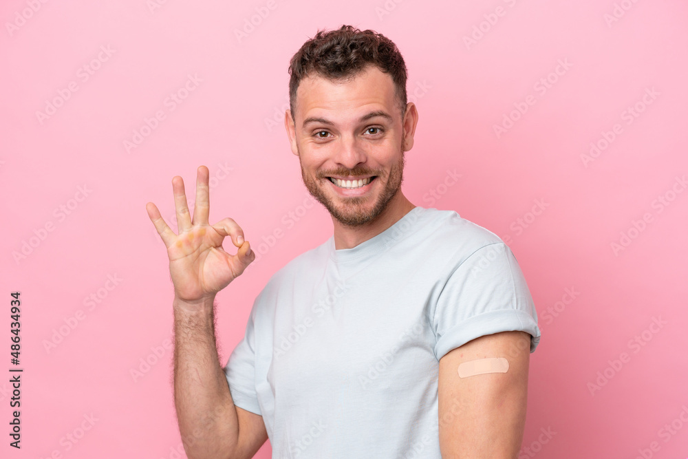 Young Brazilian man wearing a band-aids isolated on pink background showing ok sign with fingers Young Brazilian man wearing a band-aids isolated on pink background showing ok sign with fingers