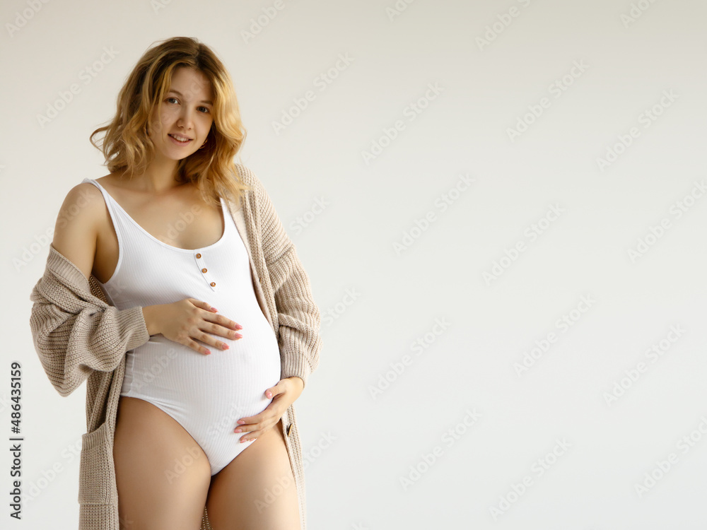 Woman standing and touching with hands her big belly. Isolated on gray background. Emotional loving pregnancy time - 37 weeks. Baby expectation. Love, happiness and safety concept. Closeup Woman standing and touching with hands her big belly. Isolated on gray background. Emotional loving pregnancy time - 37 weeks. Baby expectation. Love, happiness and safety concept. Closeup