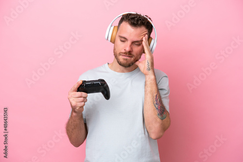 Young Brazilian man playing with video game controller isolated on pink background with headache