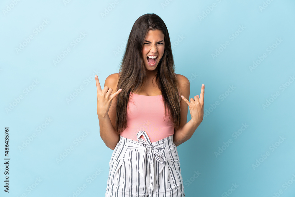 Young brazilian woman isolated on blue background making horn gesture Young brazilian woman isolated on blue background making horn gesture
