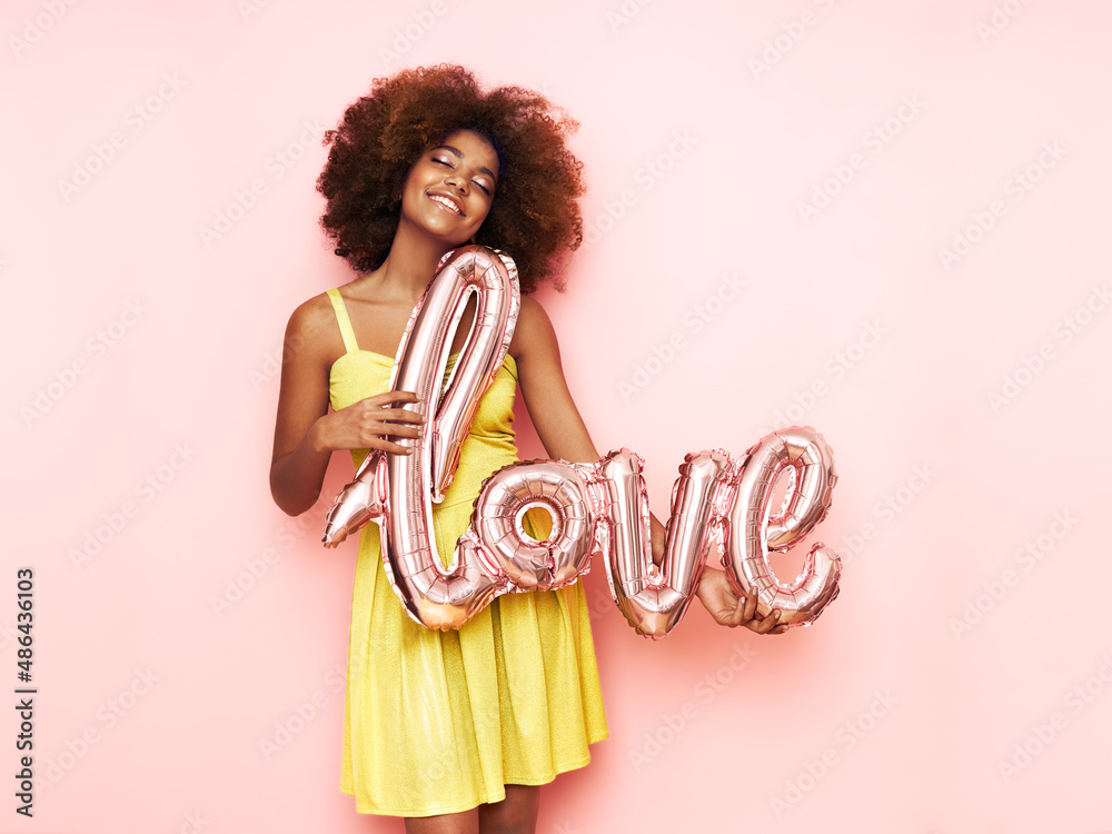 A beautiful young African-American woman with a balloon in the shape of the inscription love on a pink background. Woman on Valentine's Day. Symbol of love