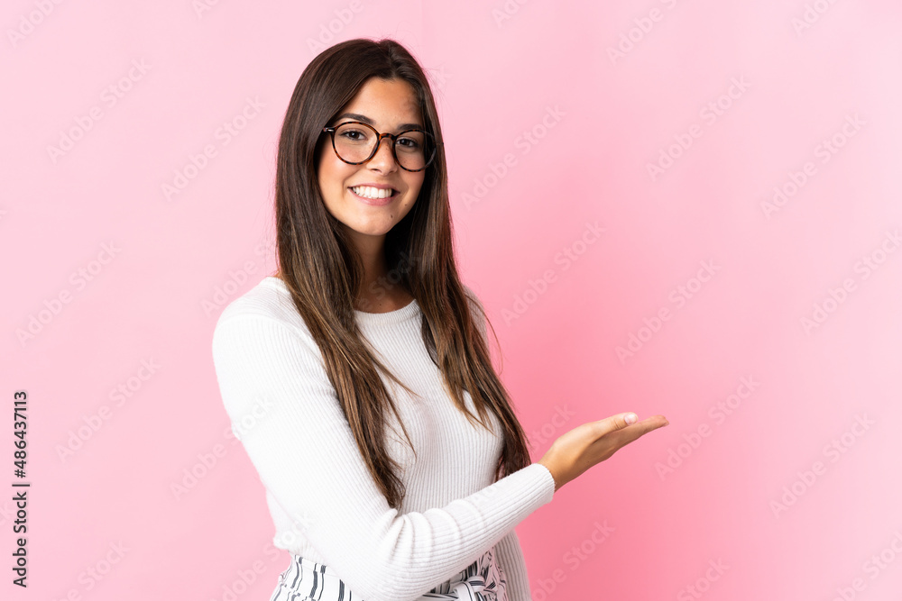 Young brazilian woman isolated on pink background presenting an idea while looking smiling towards Young brazilian woman isolated on pink background presenting an idea while looking smiling towards