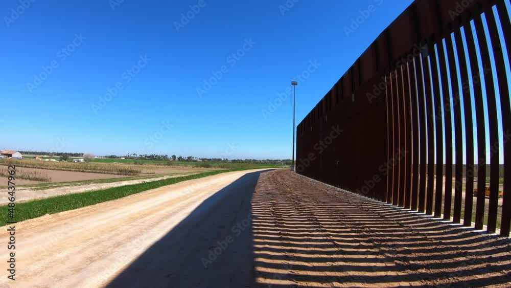 POV driving along the newly built border wall between Texas USA and Mexico; near McCallen Texas; USA farms are visible; concepts of national defense, border security, and Trump's build the wall POV driving along the newly built border wall between Texas USA and Mexico; near McCallen Texas; USA farms are visible; concepts of national defense, border security, and Trump's build the wall