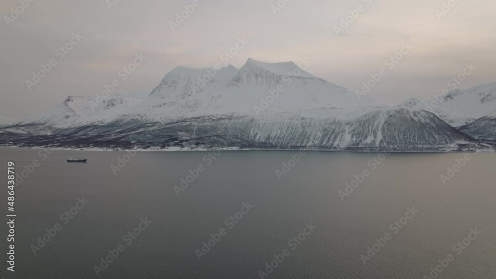 Large boat sails on coast of Norway with snowy mountains in background Large boat sails on coast of Norway with snowy mountains in background
