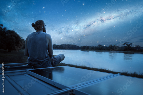 Man watching a starry night from the roof of his camper van