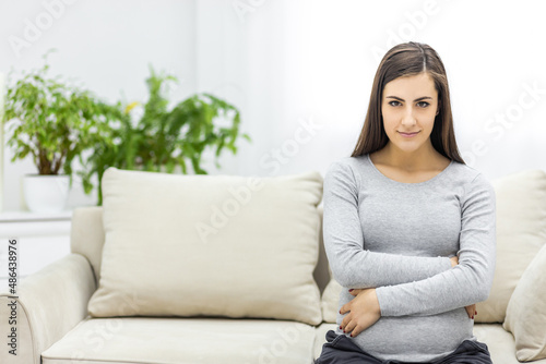 Photo of pregnant woman looking at camera and touching her stomach.