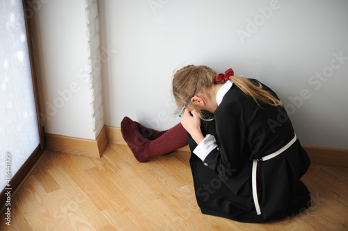 little upset school girl in black dress sitting on floor with head down on knee after education fail