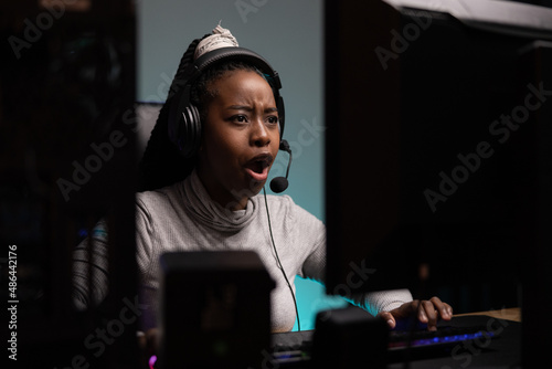 Shot from behind computer monitor of nervous pro gamer. Woman makes disgusted face talks to team members seeps headset lost game, no internet, technical problems, interrupted round of games