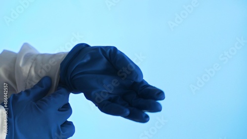 Women's hands put a second blue medical glove on their hand. Close-up on a blue background