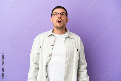 Brazilian man over isolated purple background looking up and with surprised expression