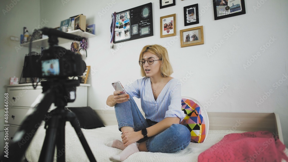 A young woman with glasses is sitting on the couch smiling, talking to the camera