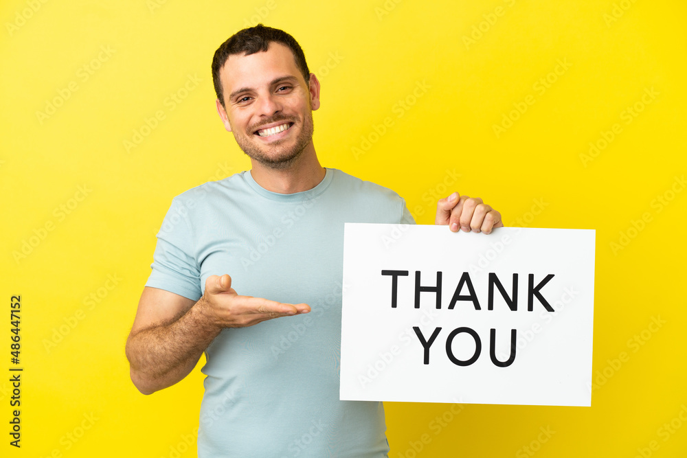 Brazilian man over isolated purple background holding a placard with text THANK YOU and pointing it Brazilian man over isolated purple background holding a placard with text THANK YOU and pointing it