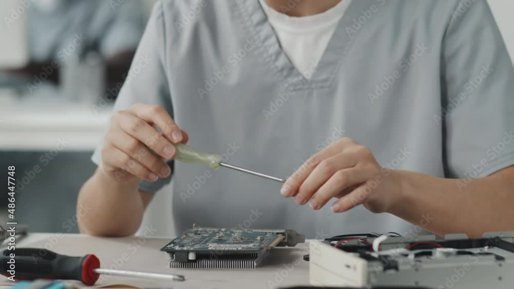 Tilt down shot of Asian female engineer using screwdriver repairing computer circuit board in laboratory Tilt down shot of Asian female engineer using screwdriver repairing computer circuit board in laboratory