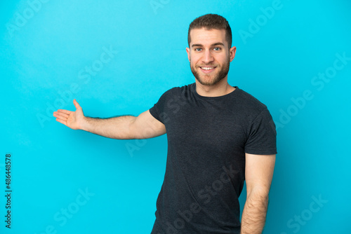 Bild auf Leinwand Young handsome caucasian man isolated on blue background extending hands to the