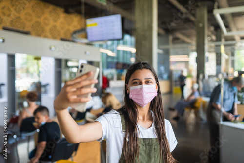Young woman in pink face mask uses smartphone at indoor.