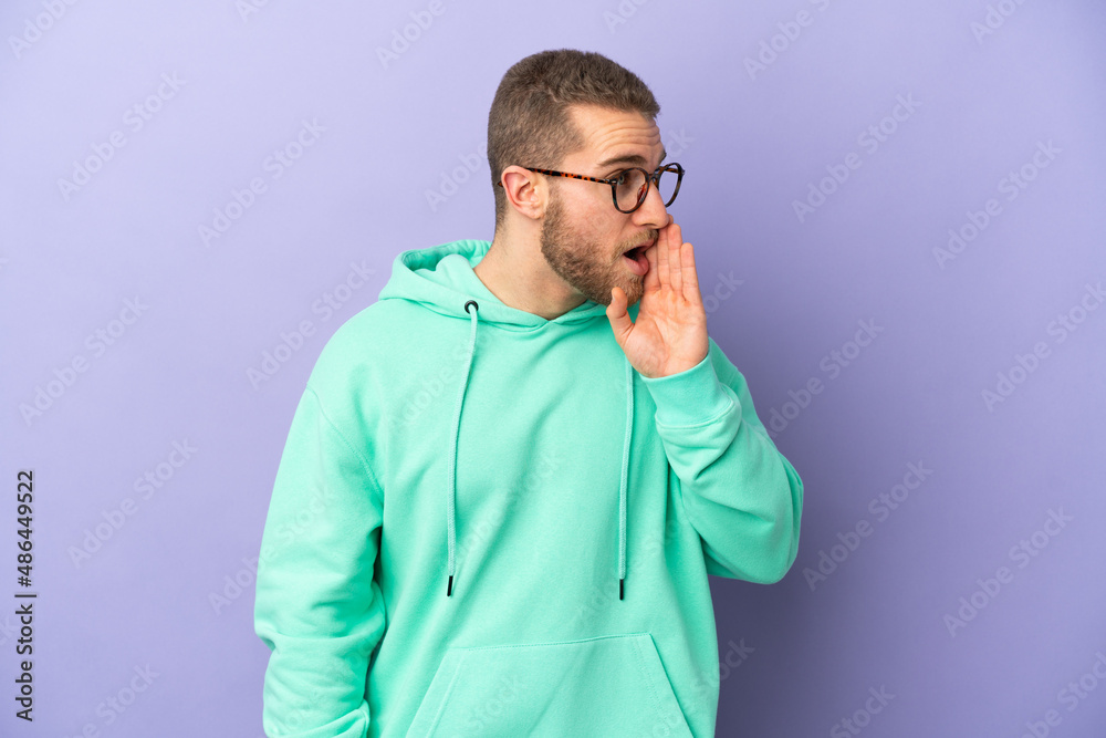 Young handsome caucasian man isolated on purple background whispering something with surprise gesture while looking to the side Young handsome caucasian man isolated on purple background whispering something with surprise gesture while looking to the side