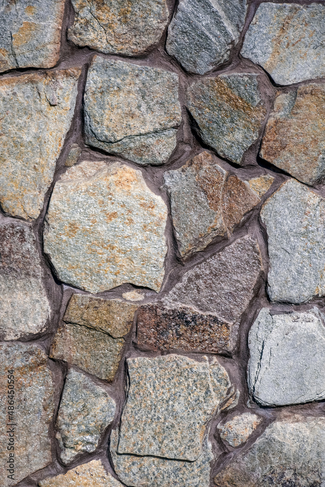 Concrete wall trimmed with wild multi-colored stone. The seams are painted with brown paint. Country style. Close-up. Selective focus. Concrete wall trimmed with wild multi-colored stone. The seams are painted with brown paint. Country style. Close-up. Selective focus.