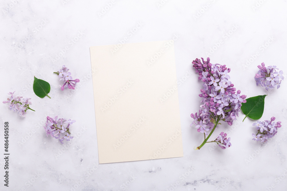Flowers composition. Sheet of paper and lilac flowers on stone background. Template for your invitation or greeting card. Flat lay, top view Flowers composition. Sheet of paper and lilac flowers on stone background. Template for your invitation or greeting card. Flat lay, top view