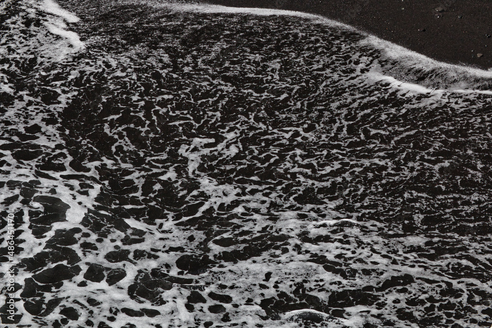 Obraz premium Spray washes over black lava sand