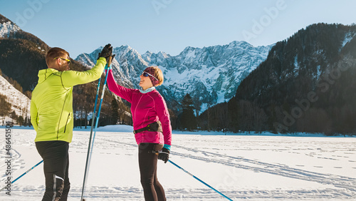 Obraz na plátně Happy middle aged couple cross country skiing giving high five and enjoying together in a beautiful mountain view