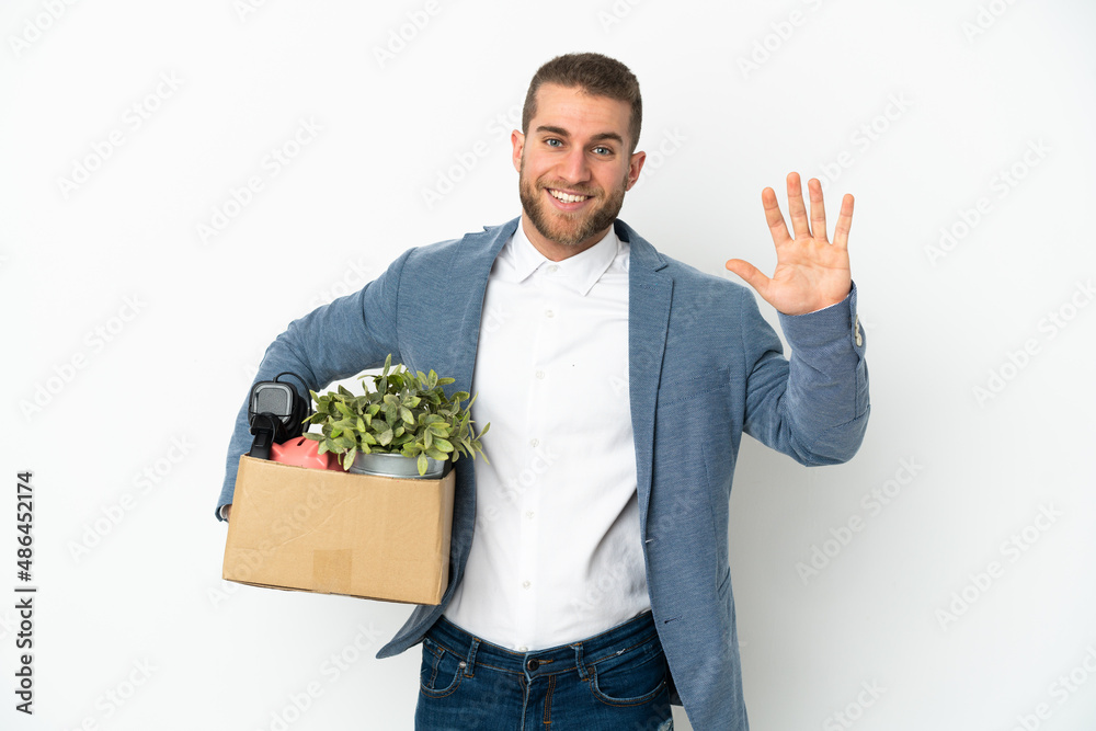 Young caucasian making a move while picking up a box full of things isolated on white background saluting with hand with happy expression Young caucasian making a move while picking up a box full of things isolated on white background saluting with hand with happy expression