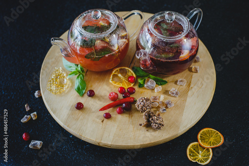 Two teapots with fruit berry tea on a round textured wooden board on a black table in a restaurant. Next to sweets, candied fruits photo