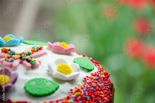 Traditional Easter cake decorated with icing and Easter decor: cross, flowers, leaves, dragee with molasses. Traditional sweets for the Christian holiday. Festive background with copy space.